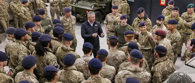 A group of uniformed soldiers wearing berets gathered around a man in civilian clothes speaking to them.
