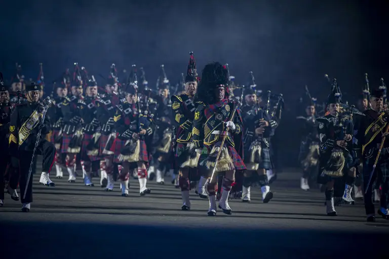 Pipes and Drummers dressed in ceremonnal uniforms, marching and playing doen the Esplanade at the Royal Edinburgh Military Tattoo..