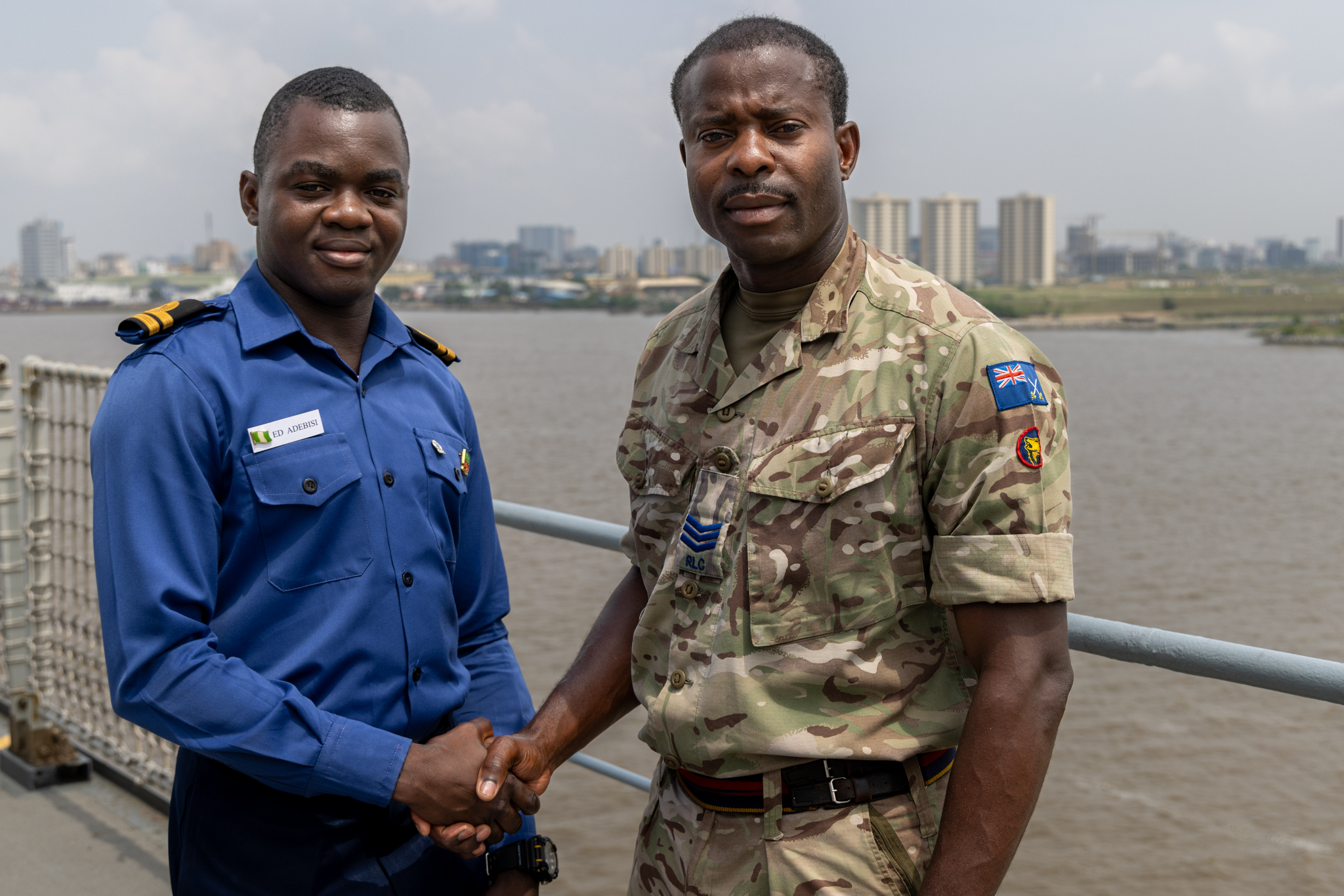 A man in a blue uniform shakes hands with a soldier in British Army uniform.