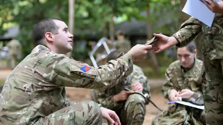 An Army clerk in camouflage uniform issues local currency to soldiers, also in camouflage uniform who have newly arrived abroad in support of Operation Gritrock.