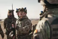 several soldiers from the Royal Regiment of Scotland are shown standing together on a training area, the main focus on a solider holding his rifle up looking at the bayonet