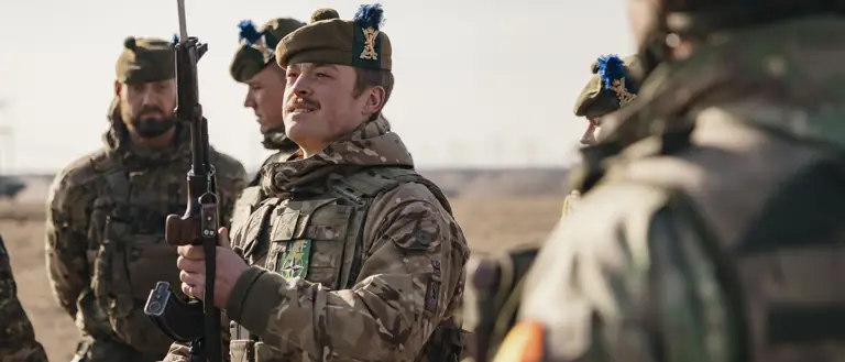 several soldiers from the Royal Regiment of Scotland are shown standing together on a training area, the main focus on a solider holding his rifle up looking at the bayonet