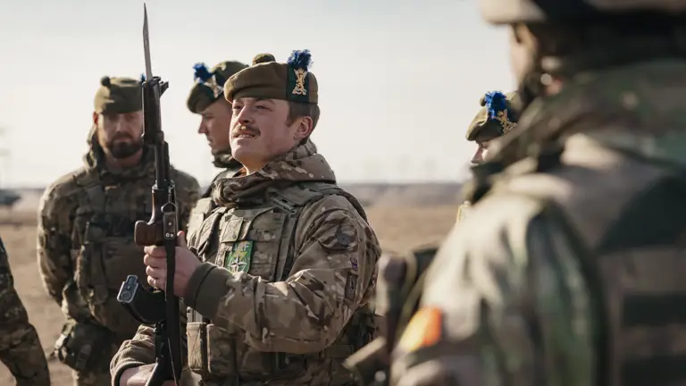 several soldiers from the Royal Regiment of Scotland are shown standing together on a training area, the main focus on a solider holding his rifle up looking at the bayonet