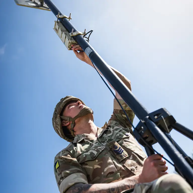 A British Army soldier climbs a communications antenna to attach a cable.