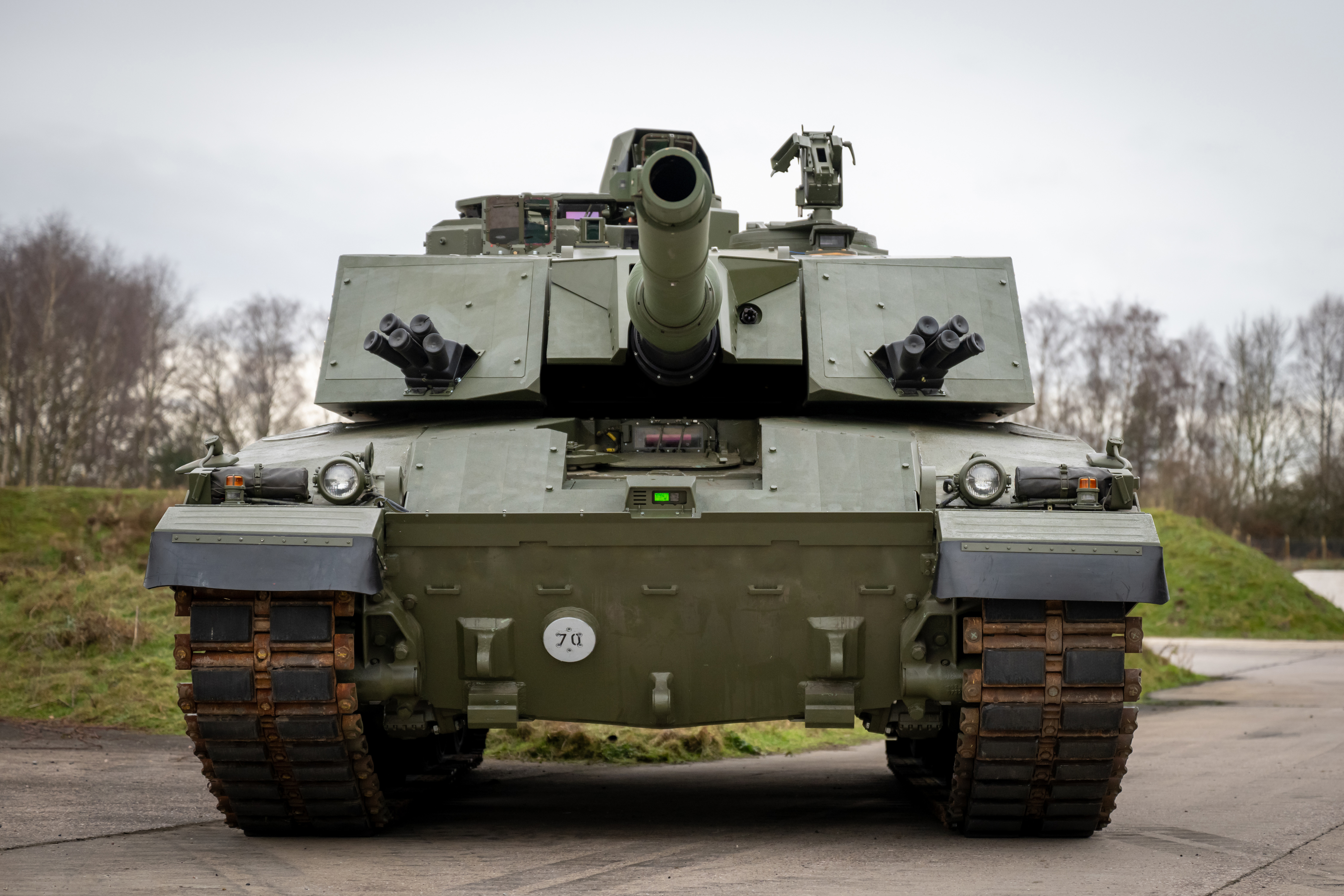 A military tank is positioned on a road, facing forward. It has a large central gun.