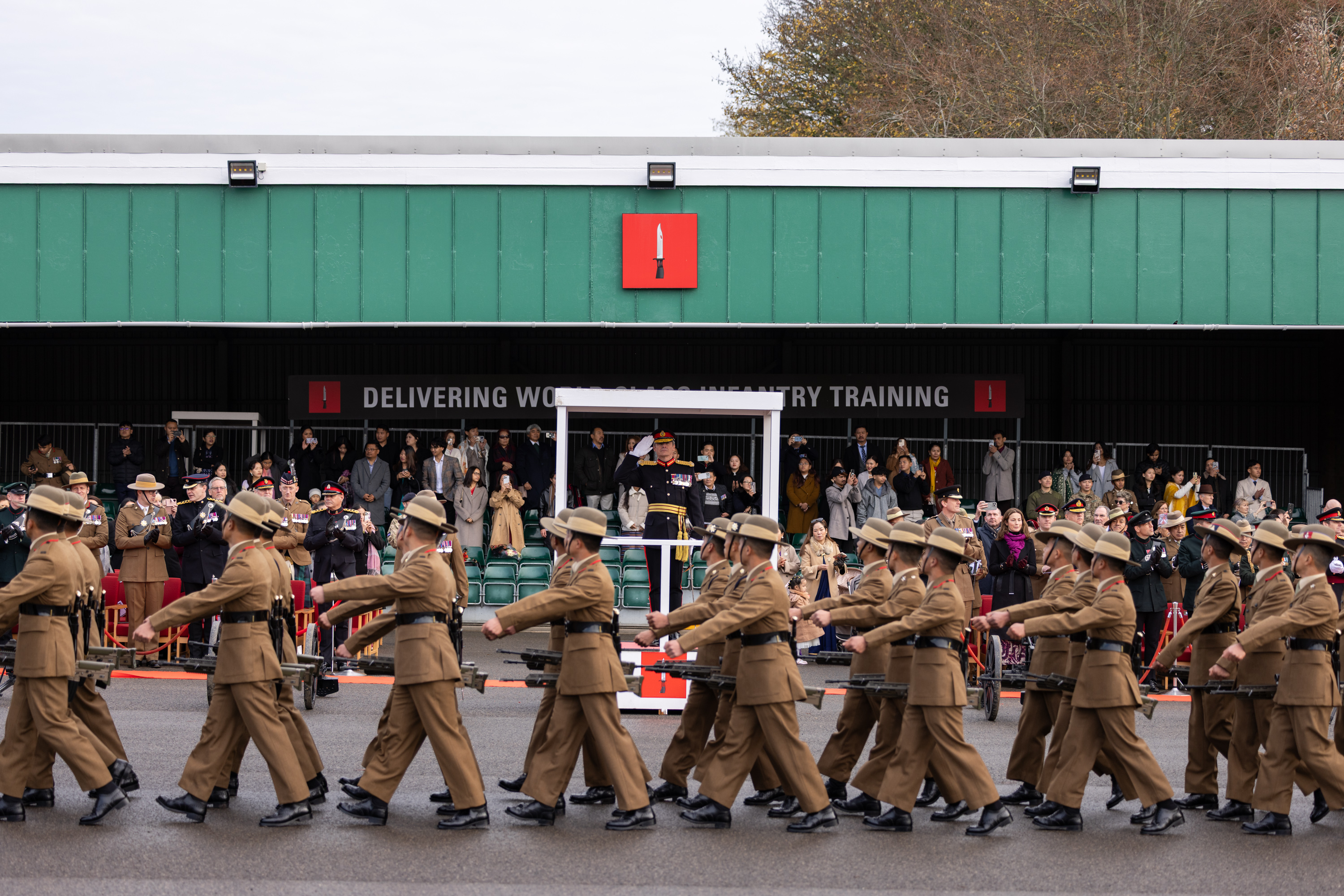 A group of uniformed individuals marches in formation outside a building.