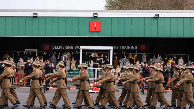 A group of uniformed individuals marches in formation outside a building.