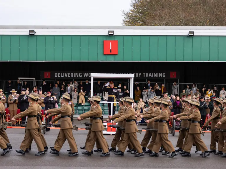 A group of uniformed individuals marches in formation outside a building.