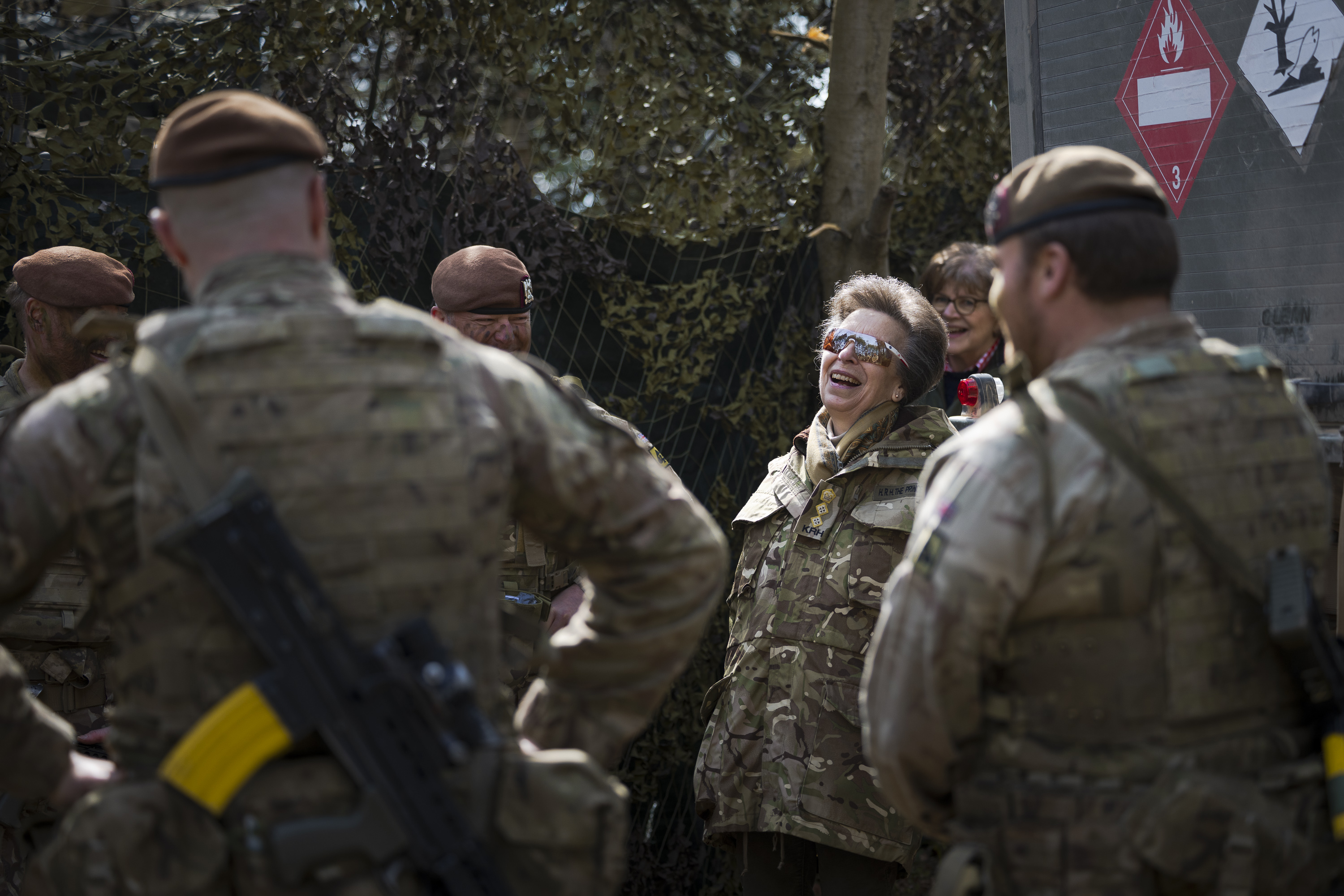 A group of military personnel in camouflage uniforms stand outdoors engaged in conversation. 
