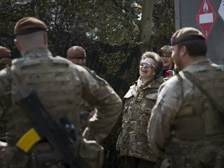 A group of military personnel in camouflage uniforms stand outdoors engaged in conversation.