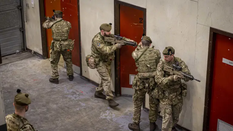 Several personnel are pictured with their weapons and they are about to enter a room in an urban environment.