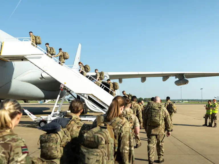 Soldiers wearing camouflage uniforms board a plane.