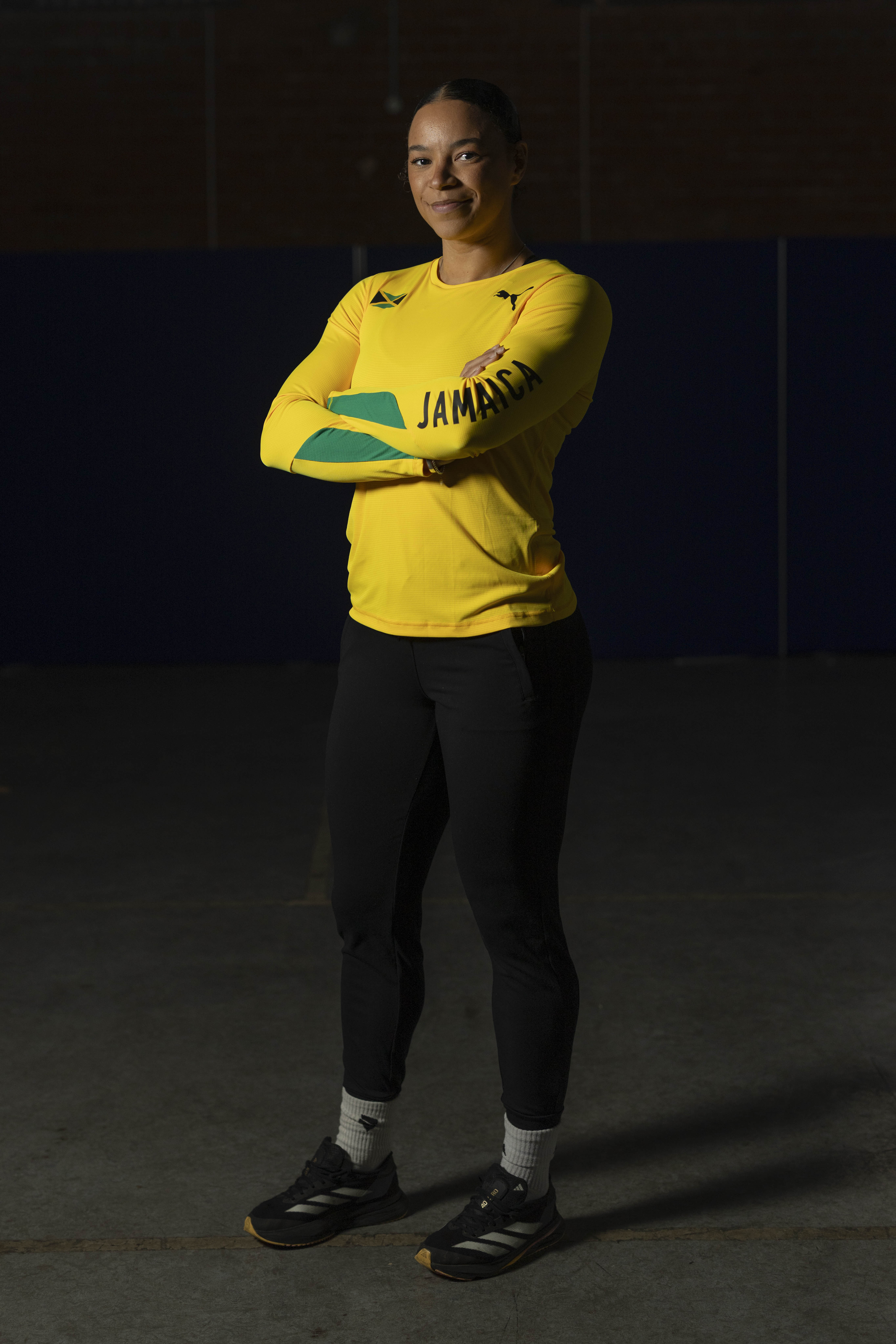 Athlete wearing a yellow long-sleeve shirt with Jamaica and Puma logos, arms crossed against a dark background.