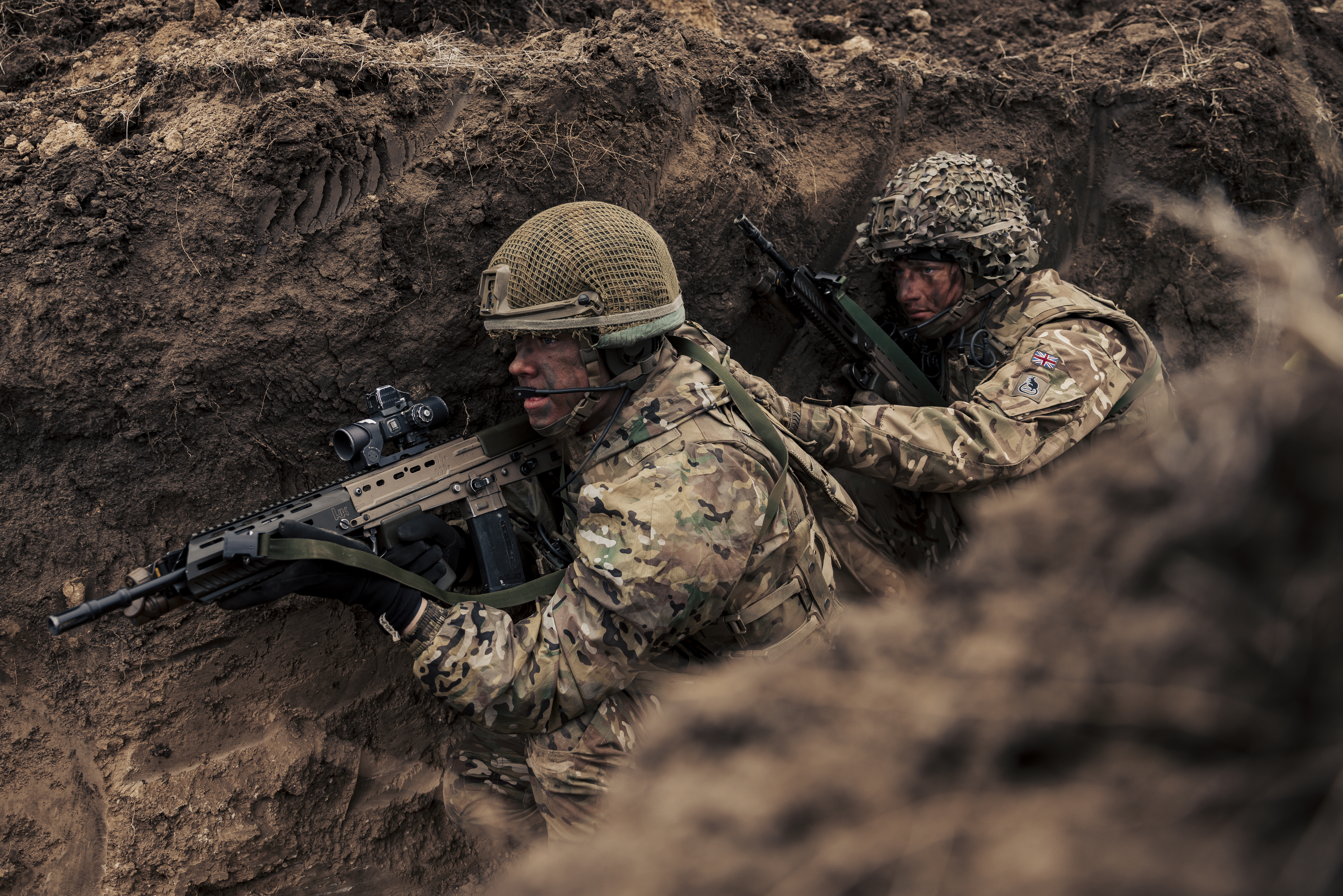 Two British soldiers in camouflage uniform with helmets and holding their rifles seen making their way through the trenches during training on Exercise Steadfast Dart 2025, 