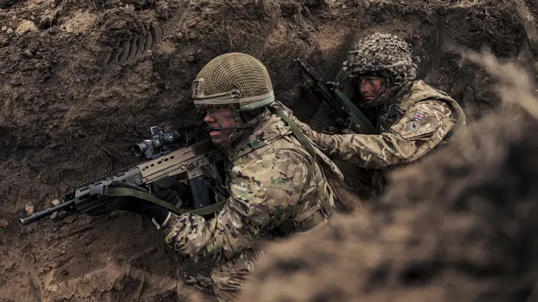 Two British soldiers in camouflage uniform with helmets and holding their rifles seen making their way through the trenches during training on Exercise Steadfast Dart 2025,