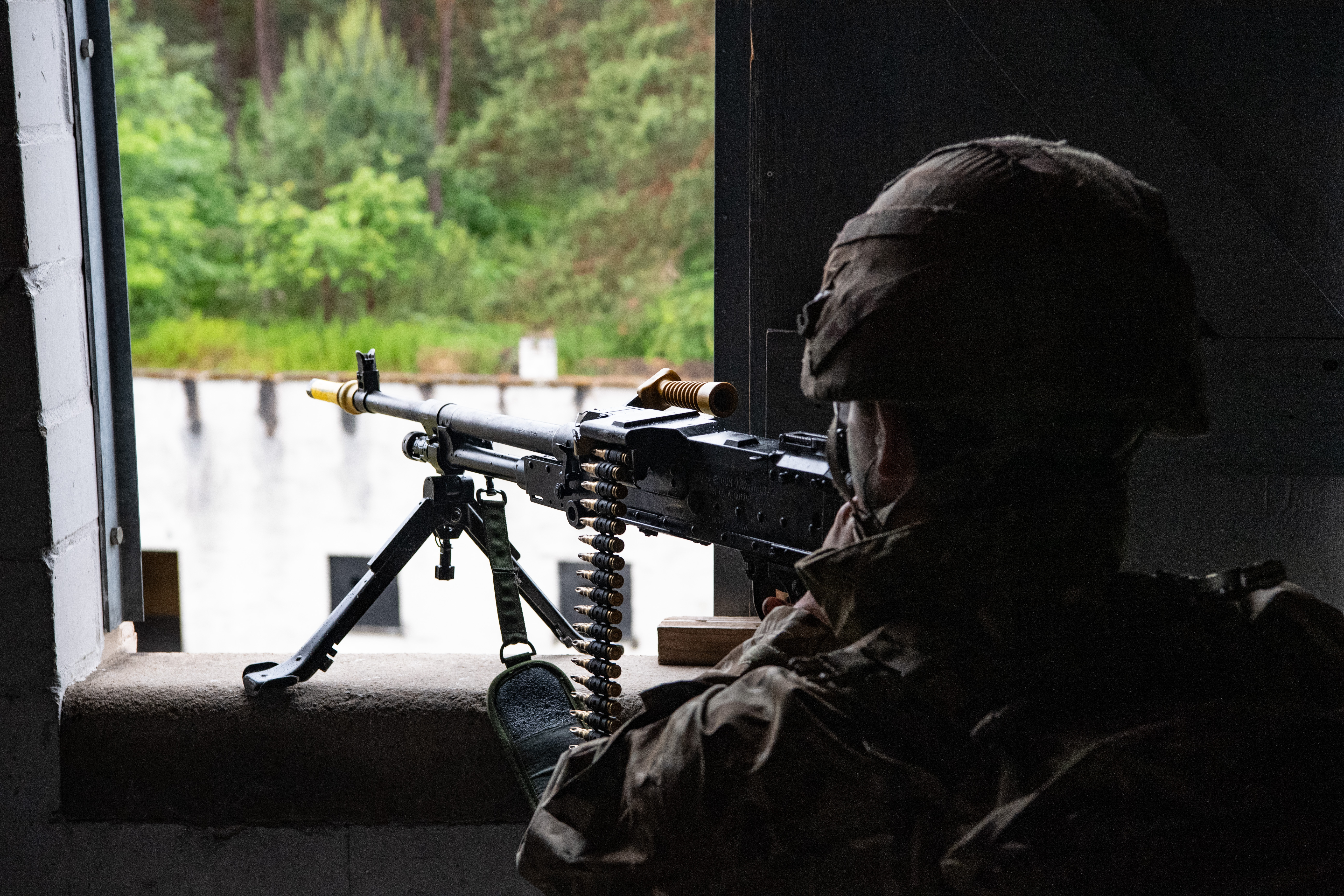 A soldiers in camouflage gear against open the window with a machine gun on a stand on the windowsill.