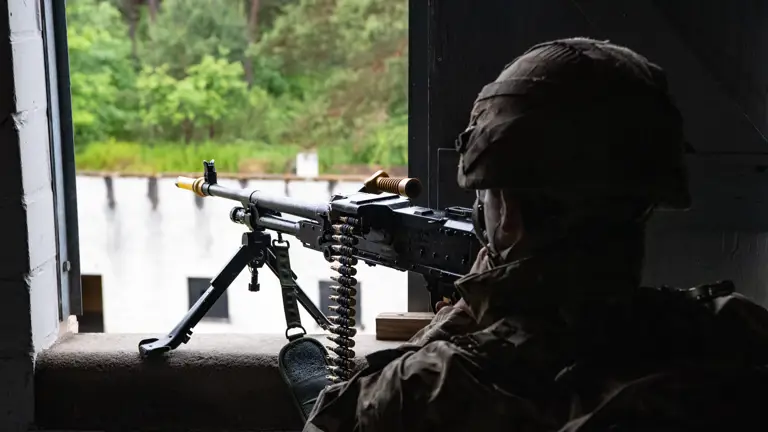 A soldiers in camouflage gear against open the window with a machine gun on a stand on the windowsill.