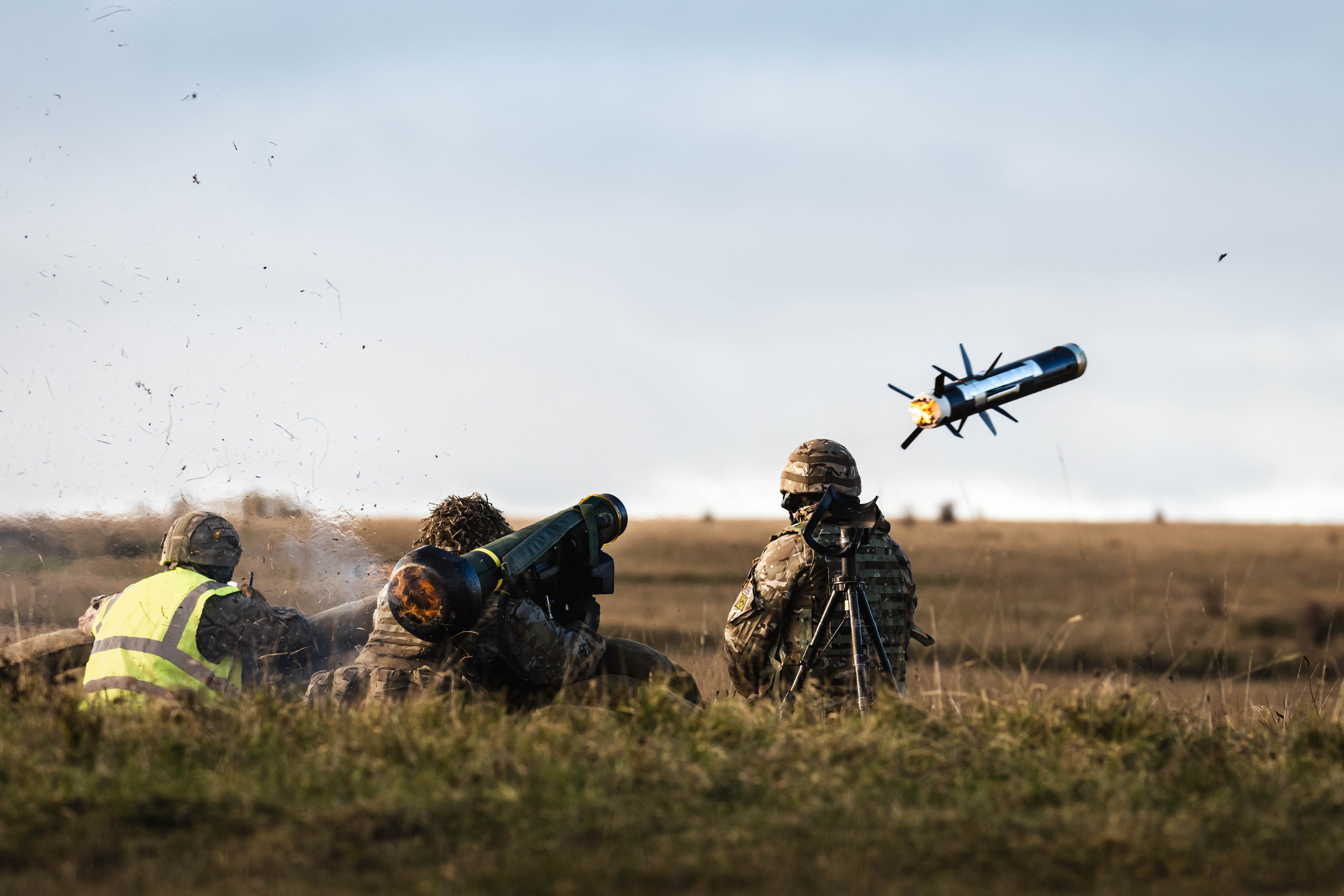 Three soldiers in uniform are positioned behind sandbags as a missile is launched from a missile launcher. 
