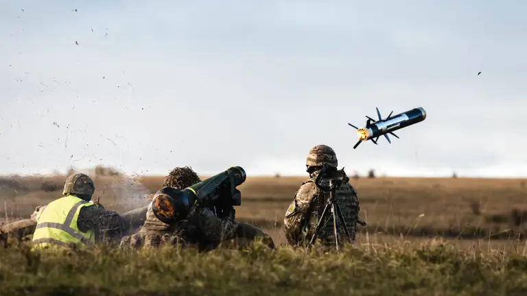 Three soldiers in uniform are positioned behind sandbags as a missile is launched from a missile launcher.