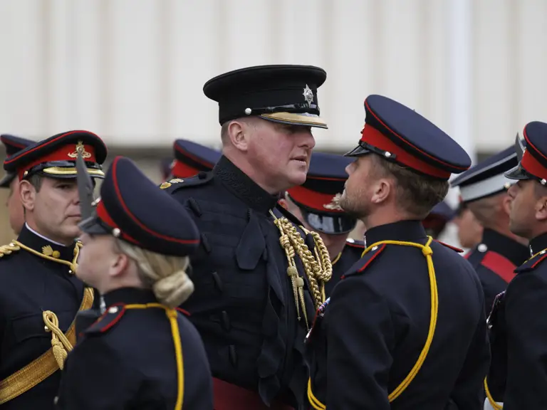 A group of uniformed individuals from the Royal Artillery stand in formation, wearing dark military attire.