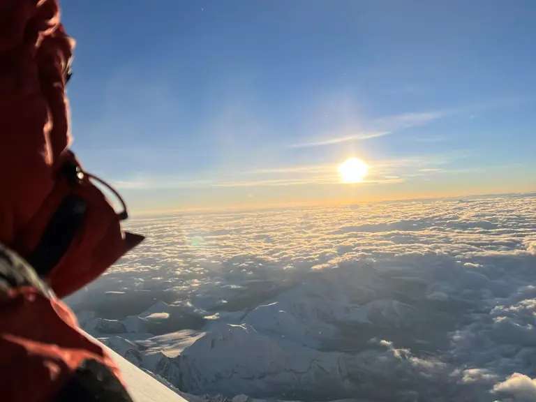 A person in in a red jacket watches the sunrise across a snowy mountain rage.