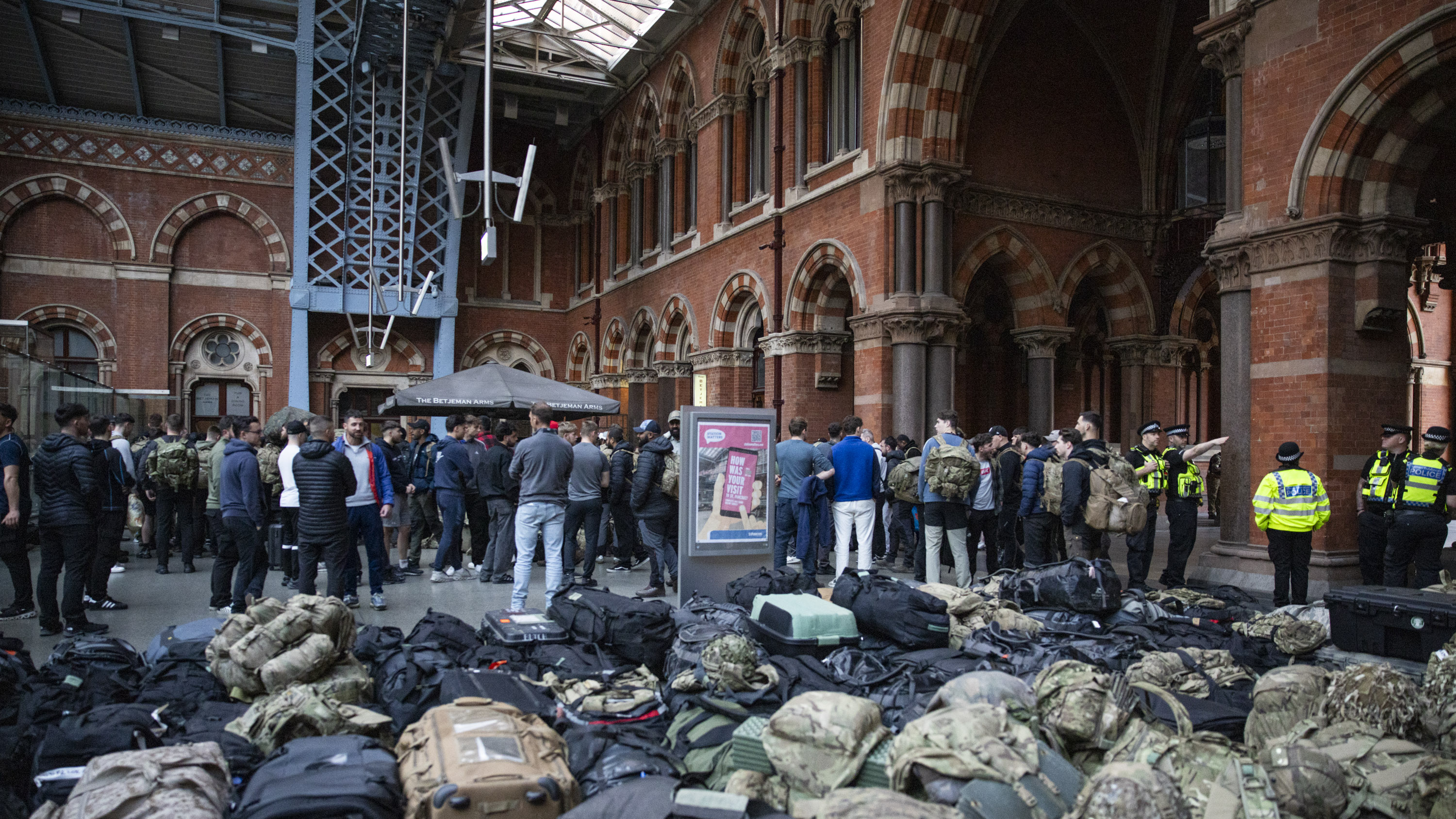 A group of soldiers stand in civilian clothing in front of all their bags in a train station.