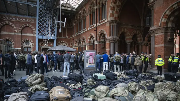 A group of soldiers stand in civilian clothing in front of all their bags in a train station.
