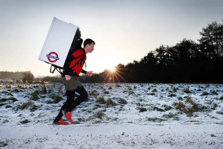Major Joss Mowforth, pictured in his workout clothes running outside in snowy weather carrying a fridge strapped to his back.