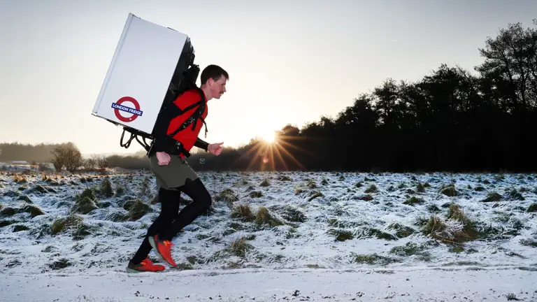 Major Joss Mowforth, pictured in his workout clothes running outside in snowy weather carrying a fridge strapped to his back.