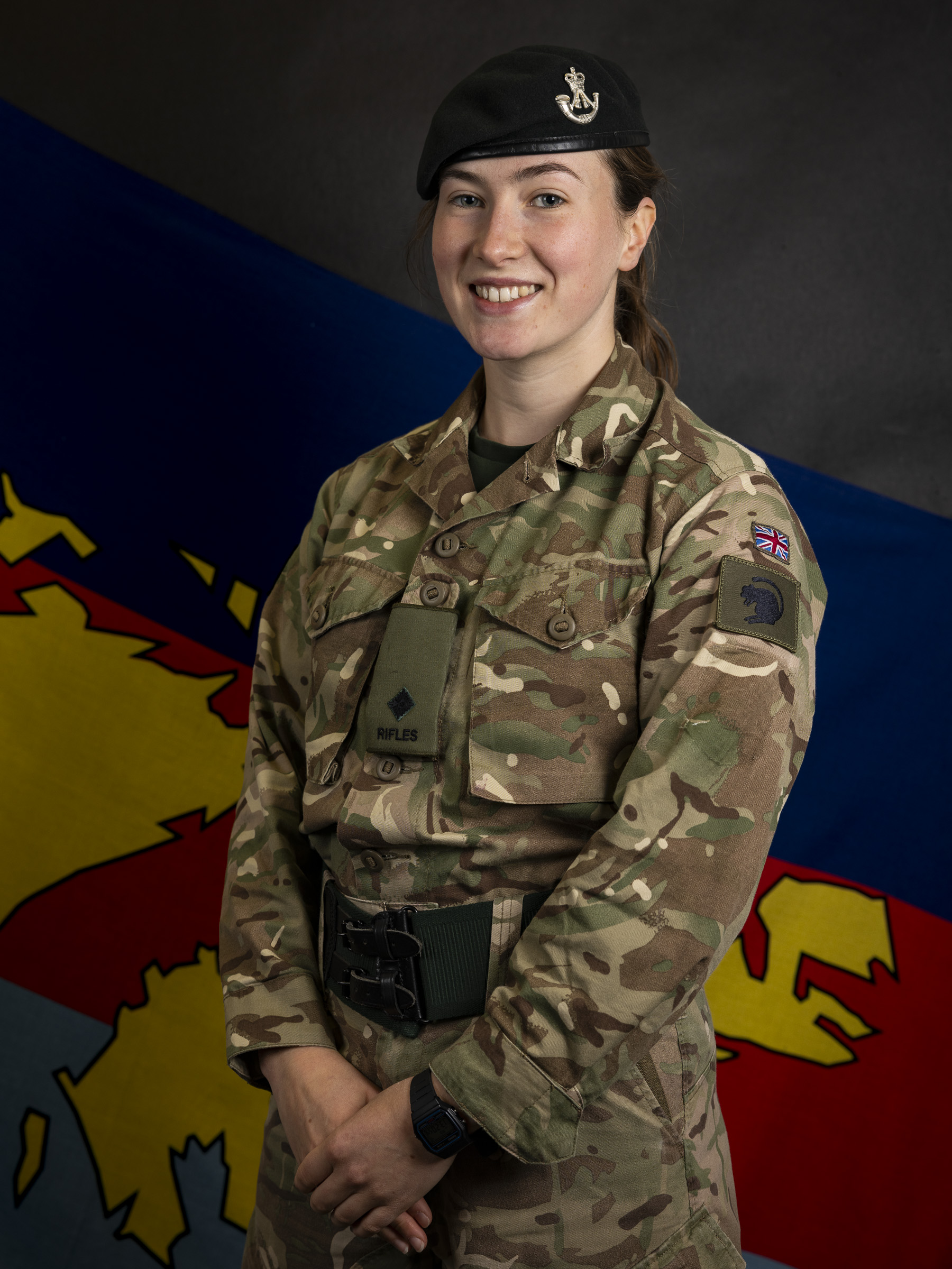 Female soldier stood posing for a portrait wearing her camouflage uniform and her navy beret on her head. 