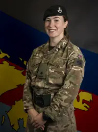 Female soldier stood posing for a portrait wearing her camouflage uniform and her navy beret on her head.