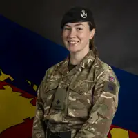 Female soldier stood posing for a portrait wearing her camouflage uniform and her navy beret on her head.