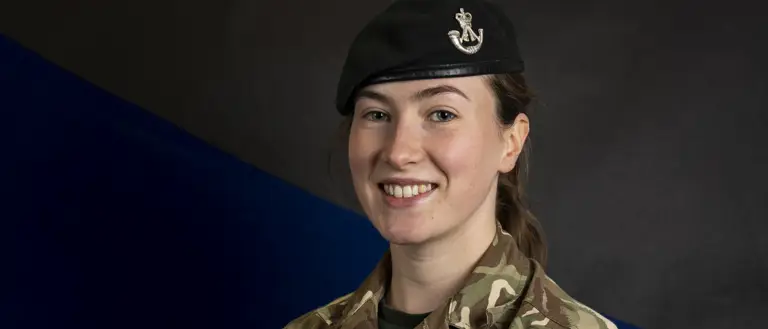 Female soldier stood posing for a portrait wearing her camouflage uniform and her navy beret on her head.