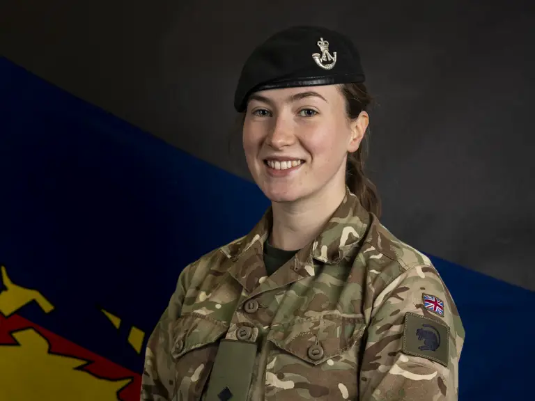 Female soldier stood posing for a portrait wearing her camouflage uniform and her navy beret on her head.