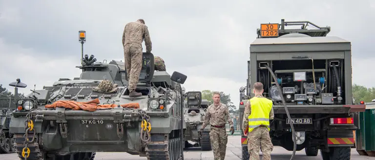 Soldiers from the British Army refuel an armoured fighting vehicle using a mobile fuel truck.