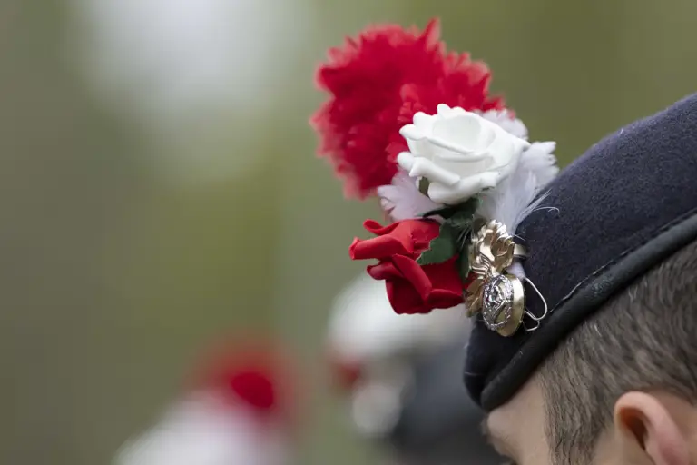 A soldier's beret with a red and white hackle, a red rose and a white rose.