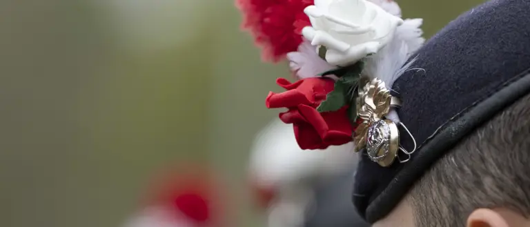 A soldier's beret with a red and white hackle, a red rose and a white rose.