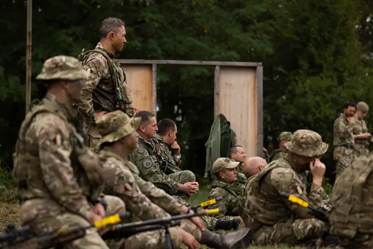 soldiers from both the British Army and the Croatian Armed Forces stand talking outside a building on exercise wearing their different camouflage uniforms