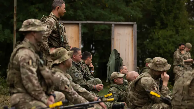 soldiers from both the British Army and the Croatian Armed Forces stand talking outside a building on exercise wearing their different camouflage uniforms