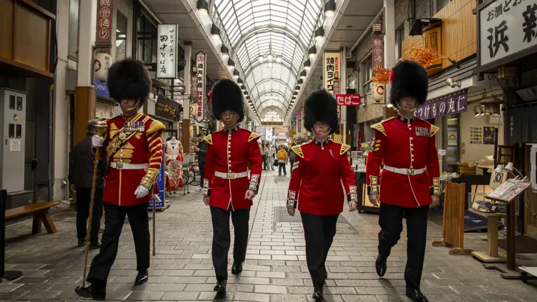 Four soldiers in red tunics and bearskin hats walk through a Japanese shopping centre.