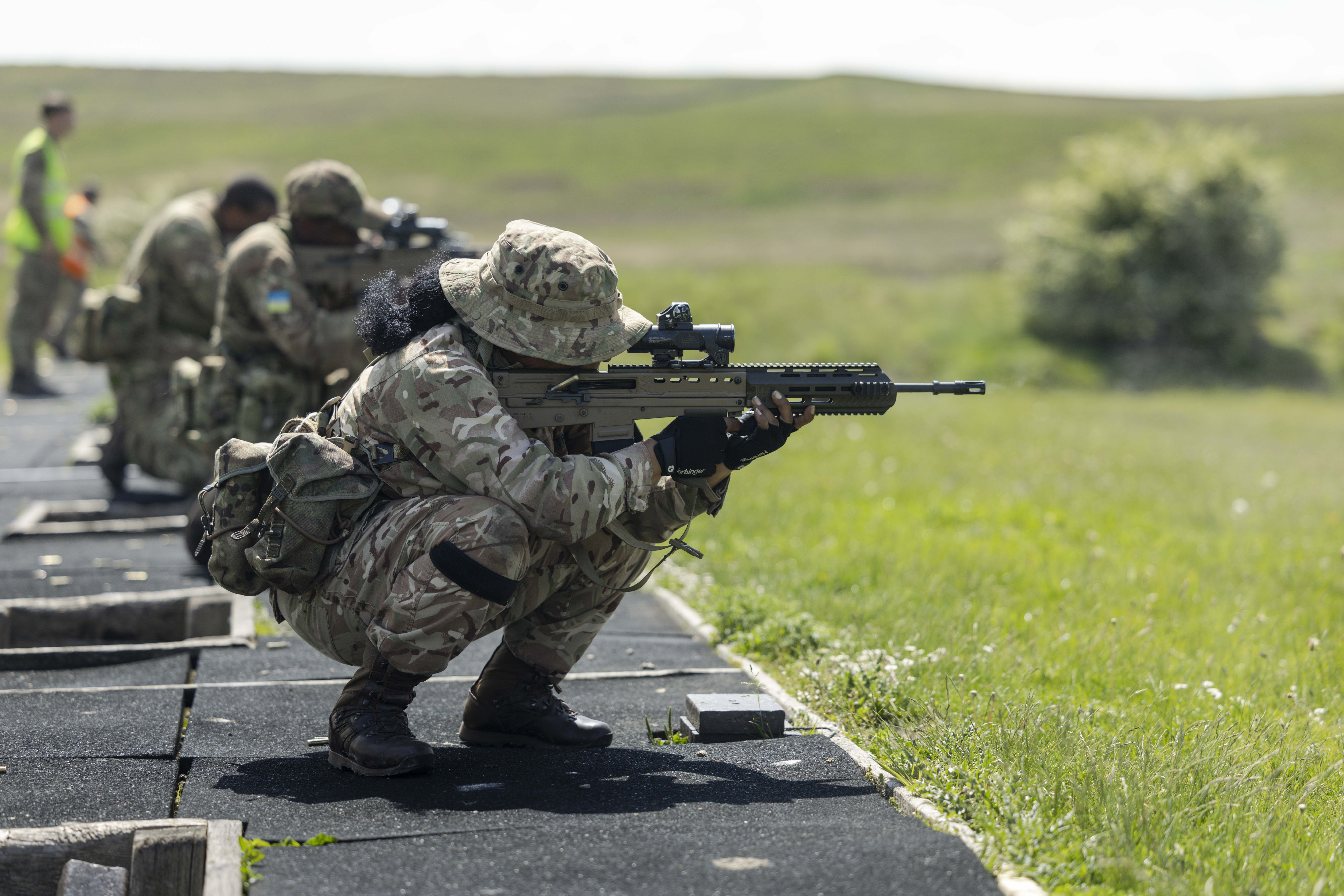 Military personnel in camouflage uniforms are training with rifles outdoors.