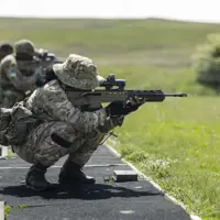 Military personnel in camouflage uniforms are training with rifles outdoors.