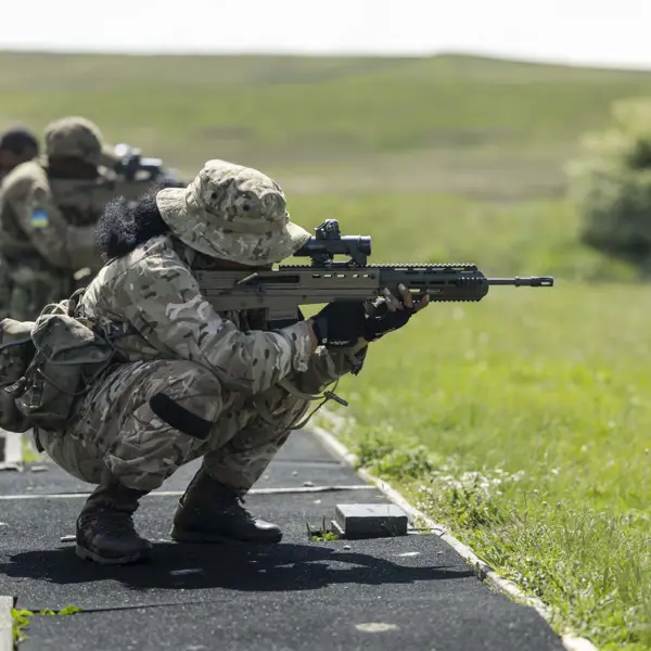 Military personnel in camouflage uniforms are training with rifles outdoors.
