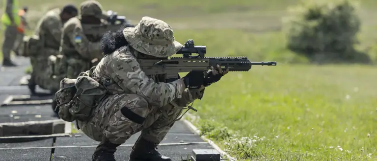 Military personnel in camouflage uniforms are training with rifles outdoors.