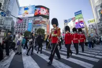Four soldiers in red tunics and bearskin hats are pictured walking across a crossing in Tokyo.