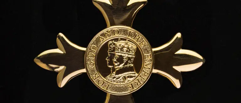 Gold medal in the shape of a cross with a crowned profile of a monarch in the centre.