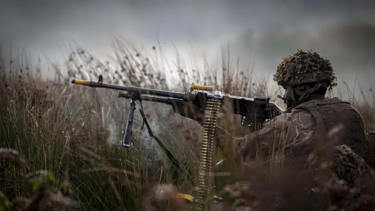 A soldier wearing camouflage uniform takes aim with a machine gun.