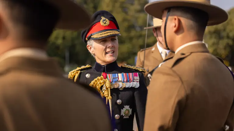 A decorated general in black ceremonial uniform inspects soldiers in brown ceremonial uniform.