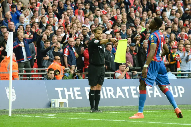 A football match scene showing an official on the side of the pitch holding a yellow flag.