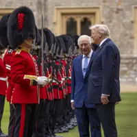 Two men in suits inspect a line of British guards dressed in traditional red uniforms and bearskin hats.